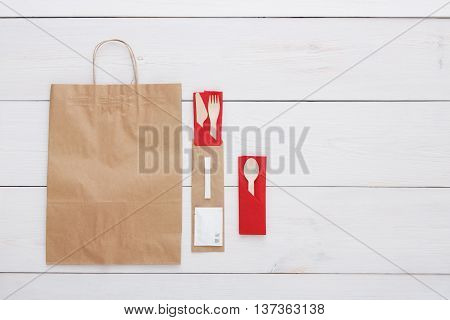 Copyspace at white wooden background for menu or recipe. Food delivery background, take away with brown paper bag. Fork and knife wrapped in paper, cutlery top view, flat lay