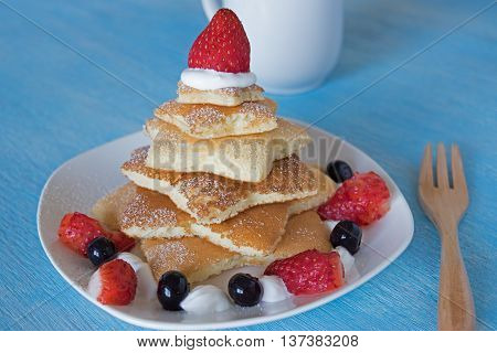 pancakes christmas tree with strawberry and blueberry in blue wooden blackground