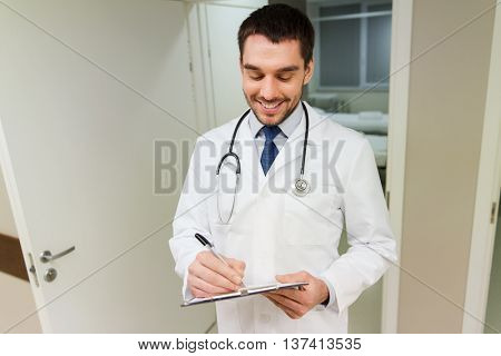 medicine, healthcare and people concept - happy smiling doctor writing to clipboard at hospital