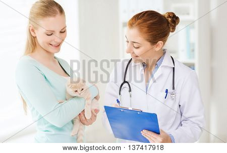 medicine, pet, animals, health care and people concept - happy woman holding scottish fold kitten and veterinarian doctor with clipboard at vet clinic