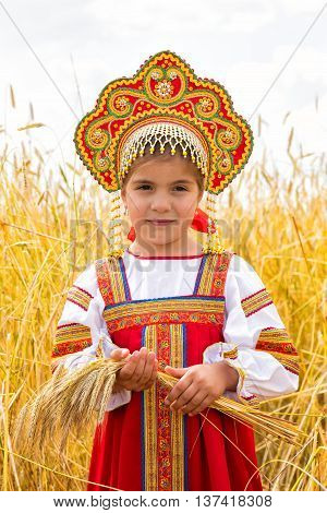 Littl girl in Russian national sarafan and a kokoshnik standing in a wheat field in summer day