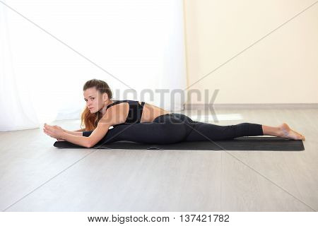 Young Woman Stretching Legs in Splits Position on yoga mat in bright room. Working on Flexbility and stretch the muscles.