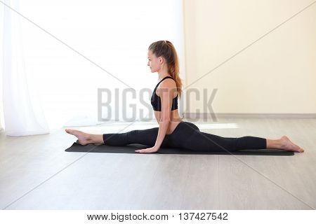 Profile happy young woman doing splitting legs apart twin in bright gym. Working on Flexbility and stretch the muscles.