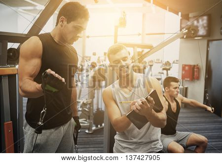 sport, fitness, lifestyle and people concept - men with clipboard taking notes and exercising on gym machine
