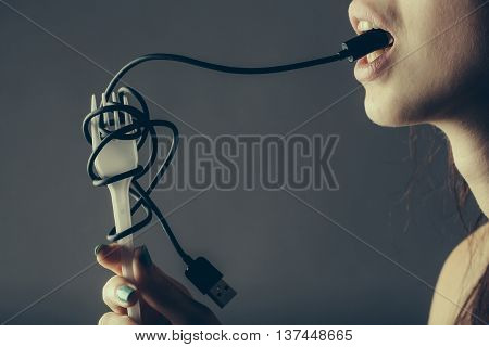 female mouth with sexy lips holding with finger usb flash wire cable for connection and white plastic fork on grey background closeup