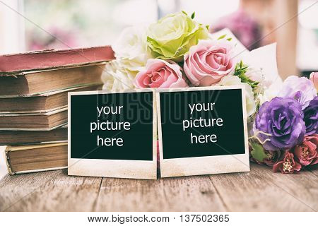 Blank vintage photo frame on wooden table with old books and flowers.Toned image.