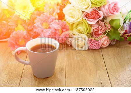 Cup of coffee on a wooden table with flower background under morning sunlight