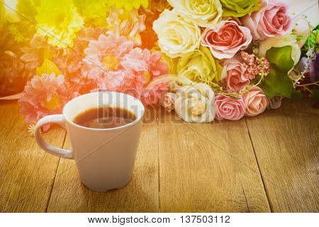 Cup of hot coffee on a wooden table with flower background under morning sunlight.Toned image.