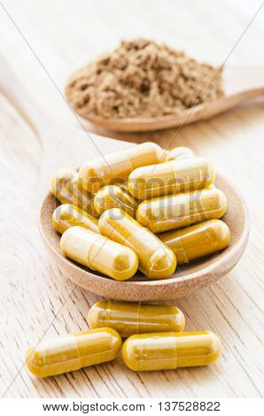 Herbal powder in capsule and wooden spoon.