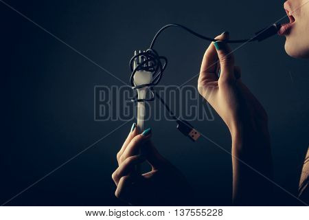 female mouth with sexy lips holding with finger usb flash wire cable for connection and white plastic fork on grey background closeup