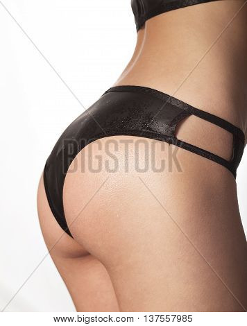 Young tanned woman with beautiful sporty buttocks and slim waistline on white wearing black sexy underwear with water drops on elastic brown wet skin No face torso