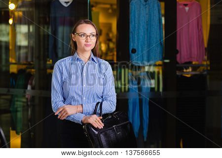 Portrait of a attractive Young Businesswoman Holding a briefcasestanding near the shop with clothing and looking away