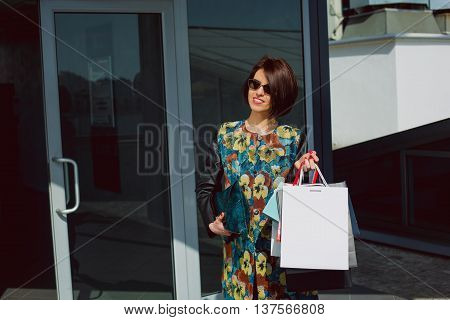 Sunny day happy women shopping. stylish girl comes out of the mall and holding bags. Fashionable and elegant style of urban clothing.