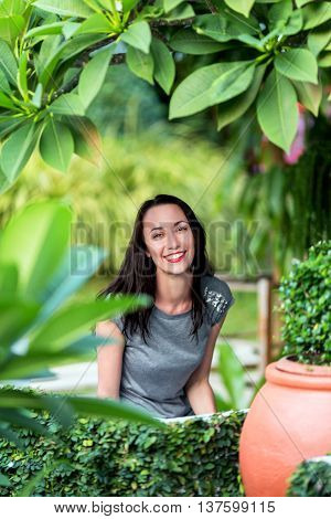 The girl sitting in the garden among the green plants and bushes, a smile on her face, Sunny day, summer