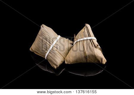 Two Zongzi or Asian Chinese sticky rice dumplings with isolated black background. Zongzi is a traditional Chinese food eaten during the dragon boat festival.
