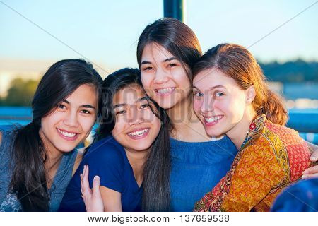 Four young women sitting together enjoying time at lake talking.