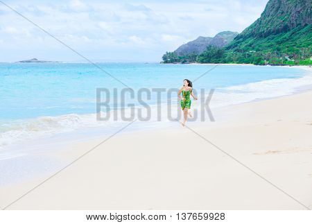 Beautiful biracial Asian Caucasian teen girl in green dress running on empty secluded Hawaiian beach
