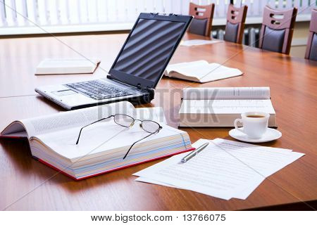 Otevřené tlusté knihy a notebook, dokumenty, brýle, pero a šálek kávy na velký dřevěný stůl wi