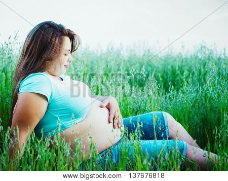 Beautiful pregnant woman sitting outdoors. Pretty pregnant woman looking at her belly and holds his hand on belly and pats belly