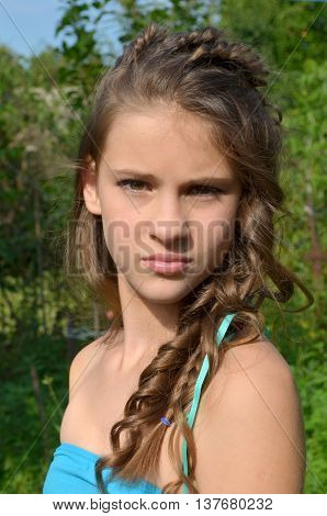 Young girl with a fine weave and long hair in the garden near blooming delphinium