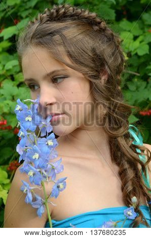 Young girl with a fine weave and long hair in the garden near blooming delphinium