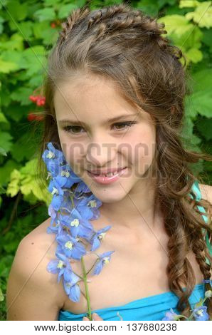 Young girl with a fine weave and long hair in the garden near blooming delphinium