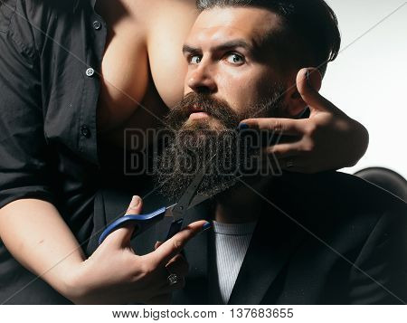 Young handsome man with long beard and moustache on serious face with female beautiful bare chest of young woman cutting with scissors