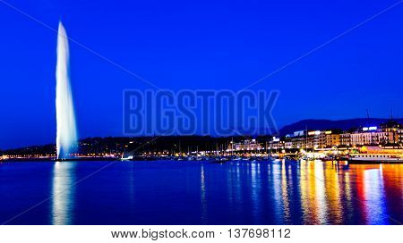 The famous national landmark Jet d'eau as seen from Jardin Anglais on a summer night. To the right is the Eaux-vives waterfront