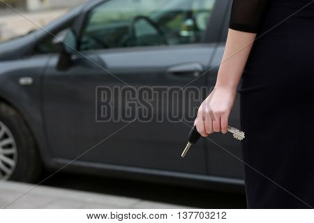 female hand holding car keys. Back view. female driver standing in front car outdoors