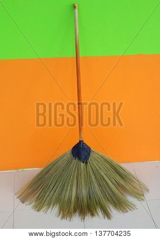 Thai fan-shaped straw broom with bamboo handle, leaning against an orange and green wall, Songkhla, Thailand
