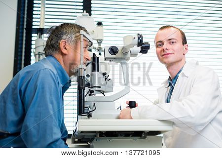 Optometry concept - senior man having his eyes examined by an eye doctor (color toned image; shallow DOF)