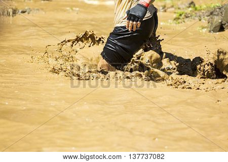 A participant is jumping into muddy water at an extreme sport challenge near Sofia. The sports event is mud and obstacle course designed to test people's physical strength stamina and mental grit.