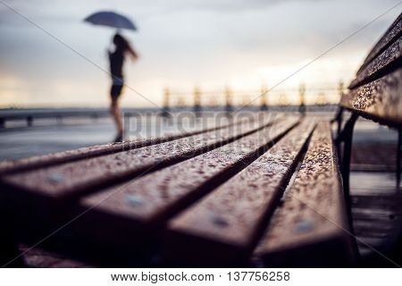 Wet bench and silhouette woman with umbrela. Rainy weather concept