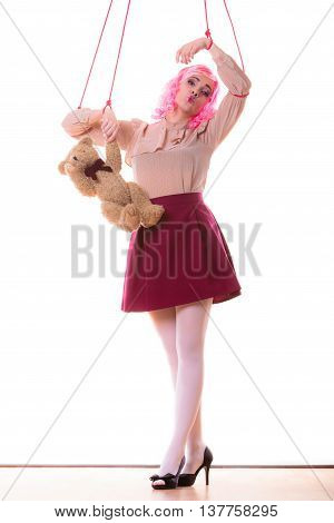 Mental disorder concept. Young woman girl stylized like marionette puppet on string with teddy bear toy isolated on white background