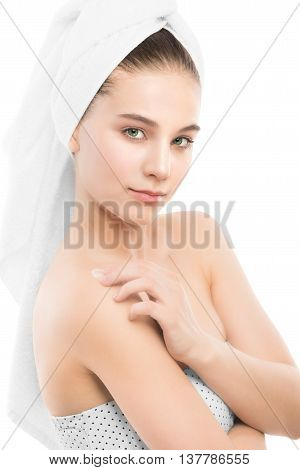 Beautiful young brunette woman with clean face and towel on her head applying moisturizer cream on shoulders. Beauty spa model girl perfect fresh clean skin. Youth and skin care concept. Isolated.