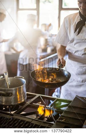 Chef tossing stir fry over large flame in commercial kitchen