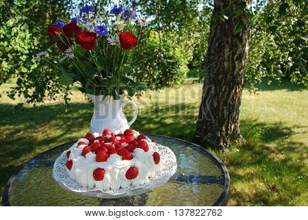 Summer decorated table with a strawberry cake and flowers in a garden