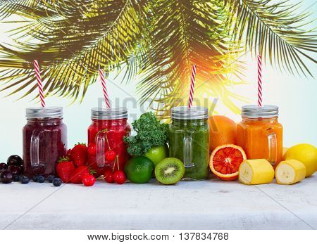 Smoothy drinks in glass jars with ingredients on white table under plam tree