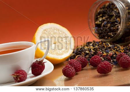 Tea lemon and red raspberry berries on a orange background