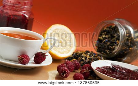 Tea lemon jam and red raspberry berries on a orange background