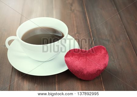 Coffee cup with heart on wood table in morning sunlight. Vintage style photo.