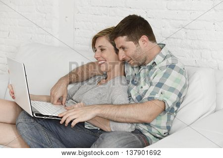 young attractive 30s couple in love sitting on couch together with laptop computer happy at home living room using the internet smiling cheerful and satisfied in technology and lifestyle concept