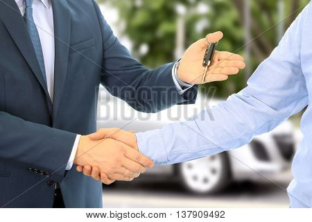 Car salesman handing over the keys for a new car to a young businessman . Handshake between two business people. Focus on a key