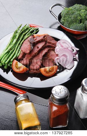 business lunch fresh roast beef meat slices on black plate wotj cutlery asparagus boiled broccoli rye bun on wooden table