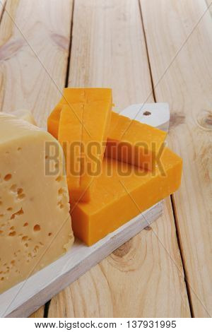 various types of fresh raw aged delicatessen cheese on white plate over light wooden table cheddar edam swiss