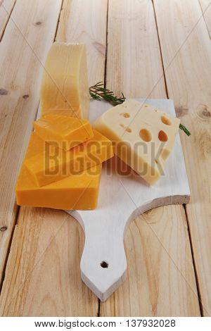 various types of fresh raw aged delicatessen cheese on white plate over light wooden table cheddar edam swiss