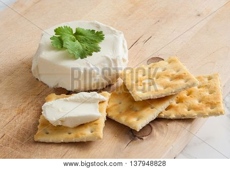 Fresh natural cream cheese with crackers on a wooden cutting board.