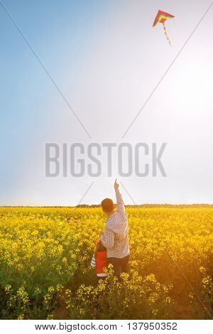 Dad and daughter launch a kite at sunset on field of yellow flower