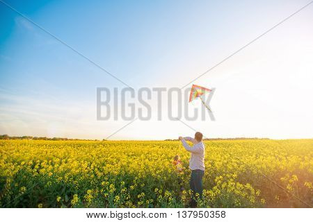 Dad and daughter launch a kite at sunset on field of yellow flower. Space for text