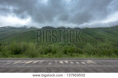 Thick Rain Clouds Cover Mounain Tops along side of Gravel Road